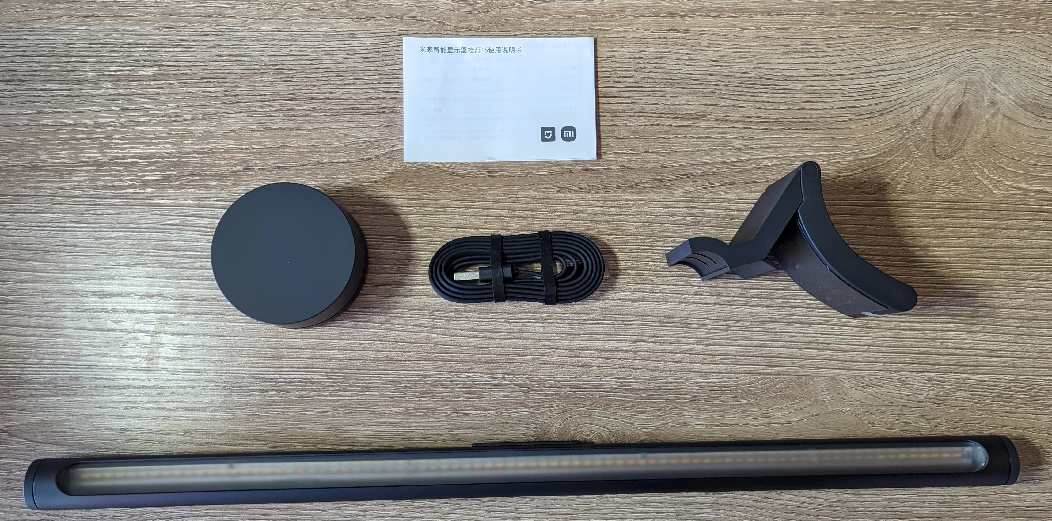 Picture showing everything that came inside the product packaging; lamp, cradle that attaches to monitor and secures the lamp, power cord, remote puck and paper instructions.